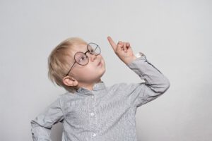  a cute blond boy with big glasses. Finger pointing up. White background.