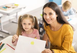 high-angle-kid-showing-her-drawing-with-her-teacher