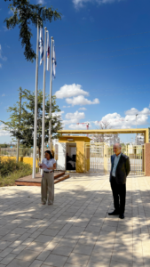 אישה מקריאה מדף ברחבת הכניסה של האקדמית חמדת, לצידה עומדים ומקשיבים נשיא המכללה ונוכחות נוספות.