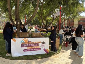 דוכן של אגודת הסטודנטים האקדמית חמדת, בו נציגות מחלקות כיבוד לסטודנטיות מתוך ארגזי קרטון תחת כיפת השמיים