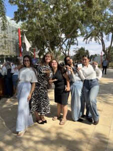 קבוצה של חמש סטודנטיות מחייכות למצלמה, חלקן מסמנות "וי" (Peace) בידיהן ואוחזות בצלחות כיבוד קטנות, במהלך אירוע חברתי בקמפוס